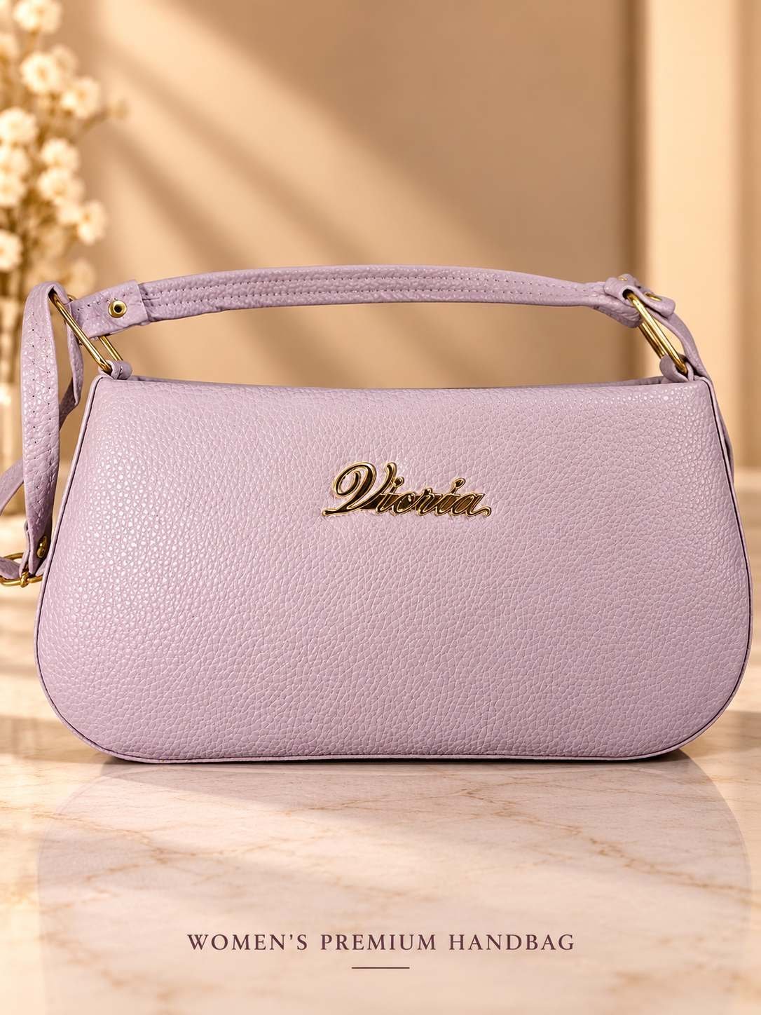 Women's lavender pebbled-texture shoulder bag with gold-tone script emblem, short top handle and two zipped compartments
